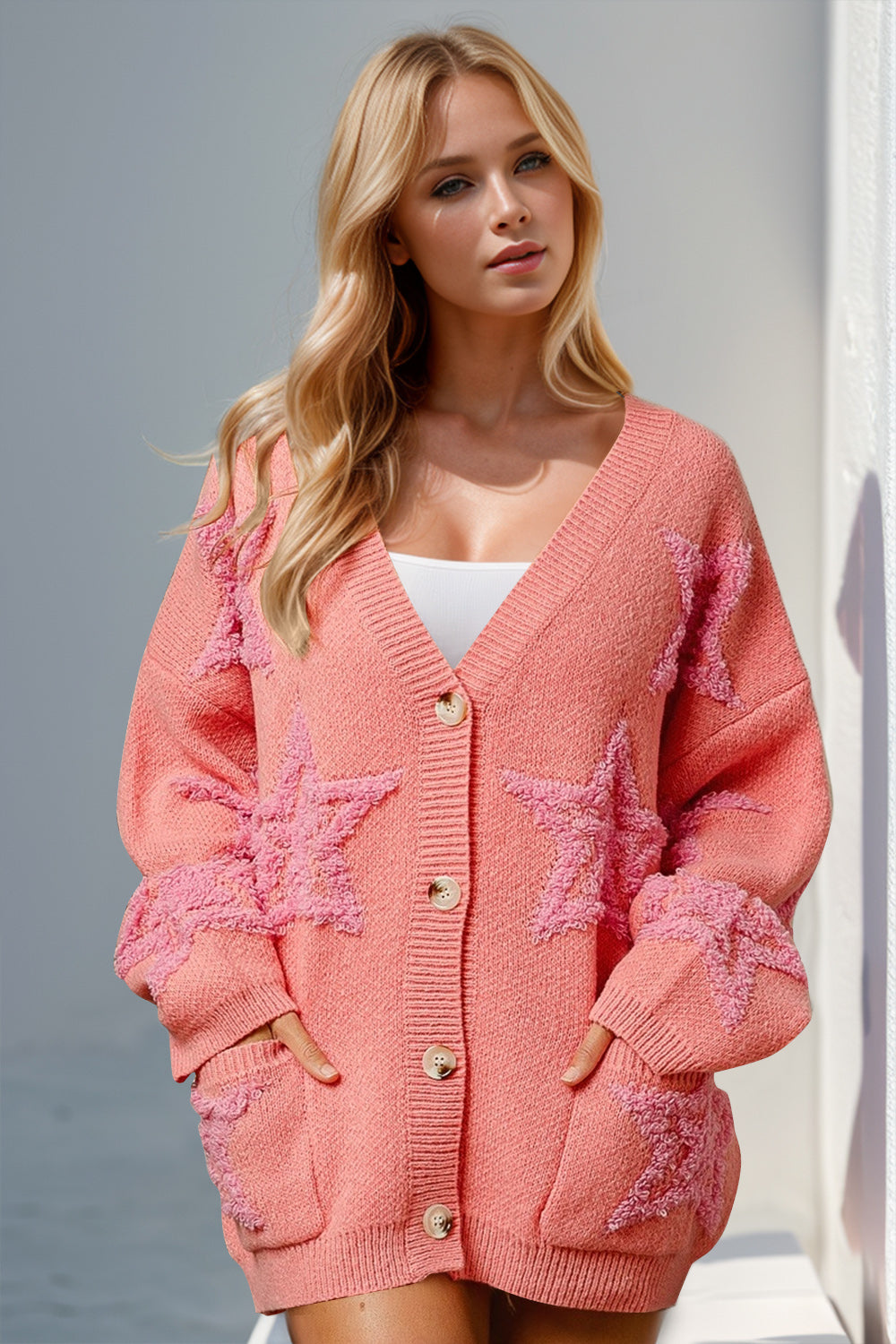 A woman wearing a beige knitted cardigan with a star pattern, featuring button-up front and a round neckline.